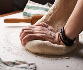 person making dough beside brown wooden rolling pin