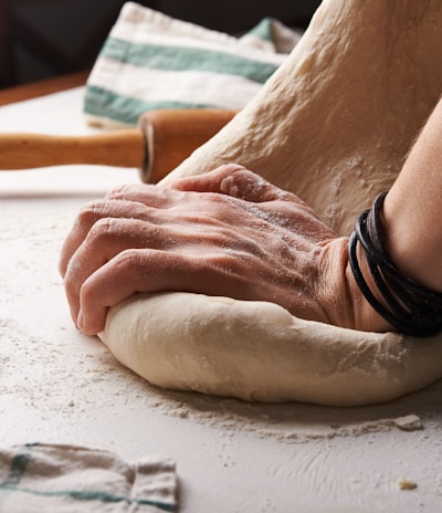 person making dough beside brown wooden rolling pin