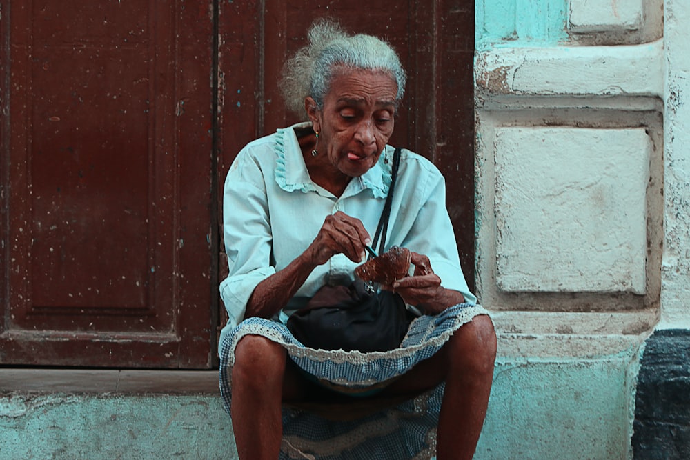 茶色の木製のドアの近くの灰色のコンクリートの地面に座っている女性