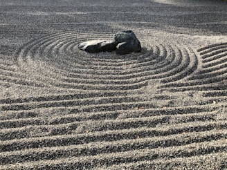 A Zen garden with meticulously raked gravel creating concentric circular patterns around a group of large stones, evoking a feeling of tranquility and order.