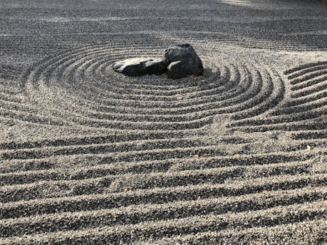 A Zen garden with meticulously raked gravel creating concentric circular patterns around a group of large stones, evoking a feeling of tranquility and order.