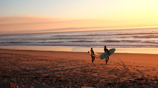 two surfers walking on sand going on water
