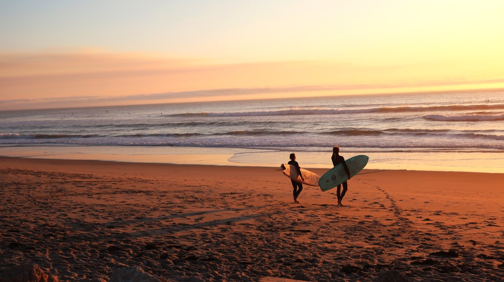 Dos surfistas caminando sobre la arena yendo sobre el agua