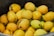A collection of ripe mangoes with a mix of yellow and green colors, some showing dark spots, piled together in a black container.