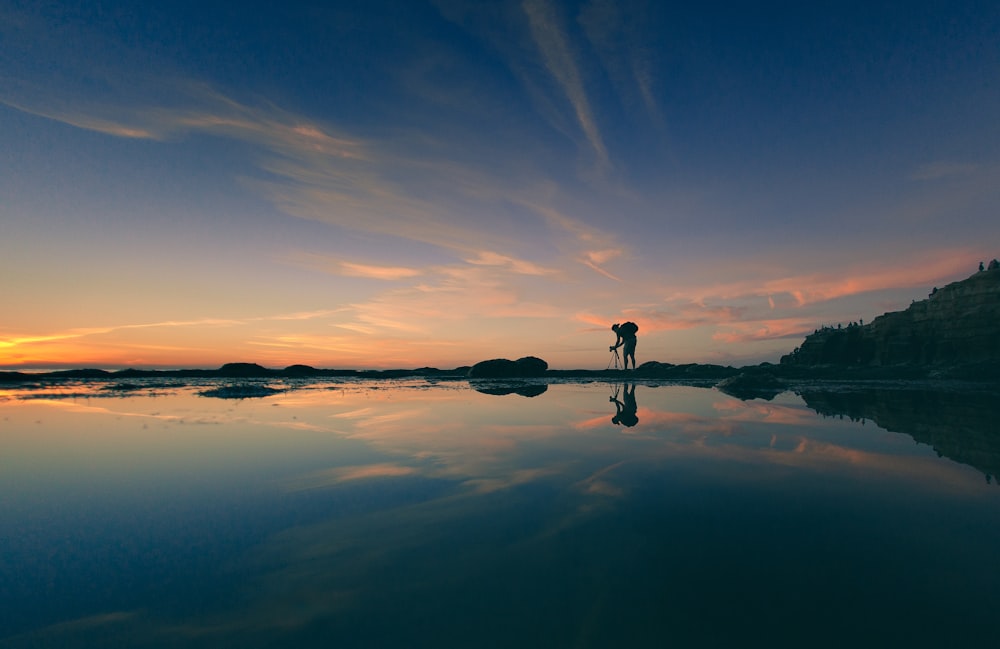 landscape photography of man adjusting camera tripod during golden hour