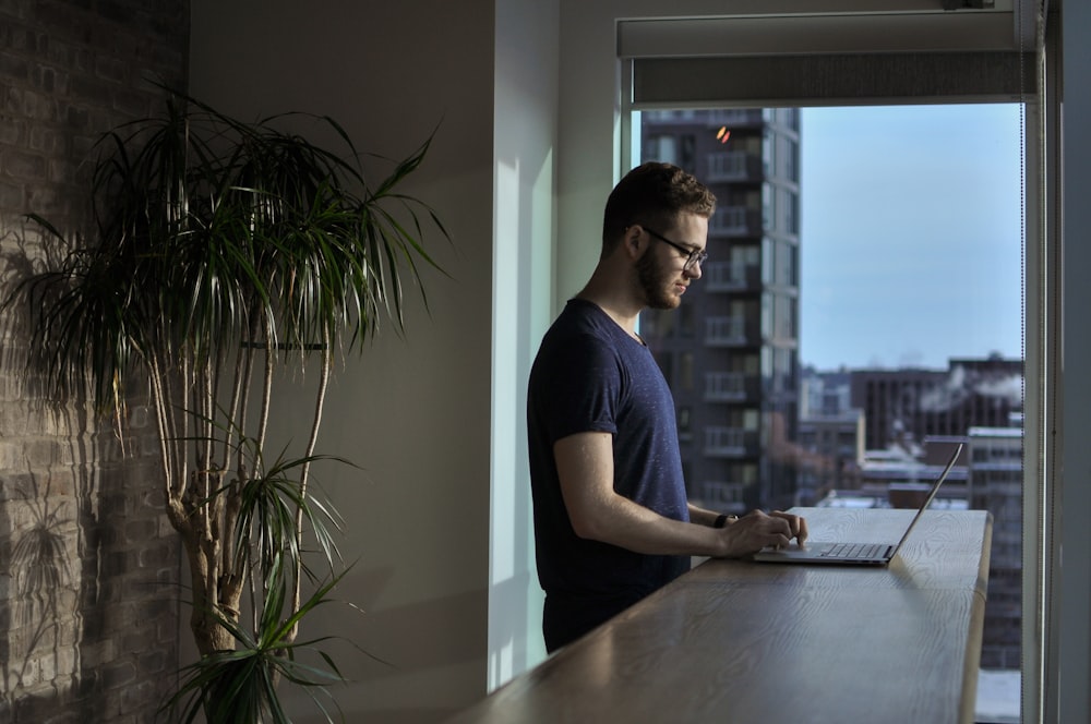 hombre de pie al lado de la mesa usando una computadora portátil