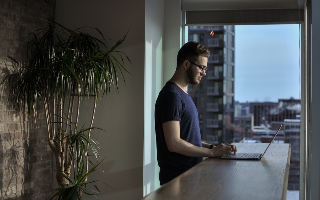 man standing beside table using laptop