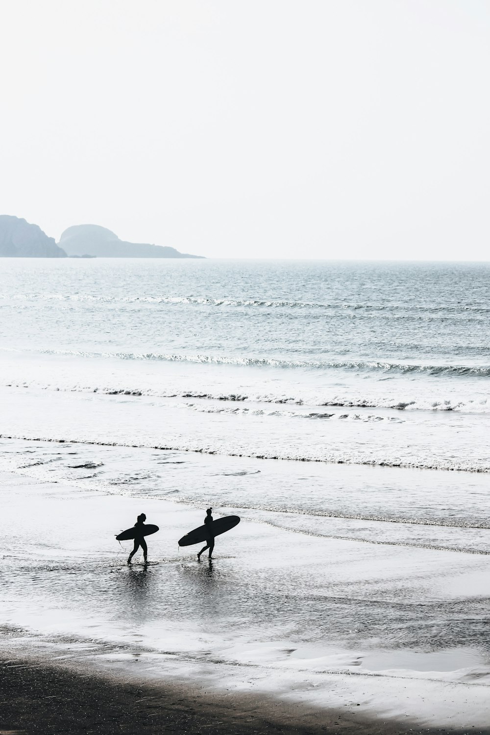 낮에 해변에서 서핑 보드를 운반하는 두 사람