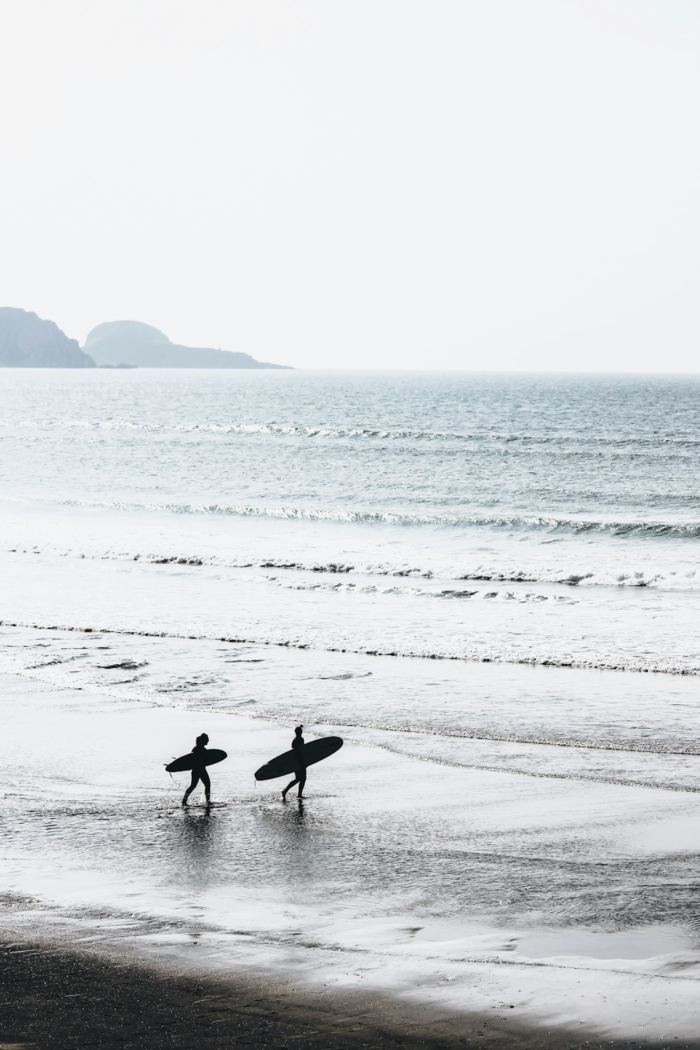 Dos personas cargando tablas de surf en la playa durante el día