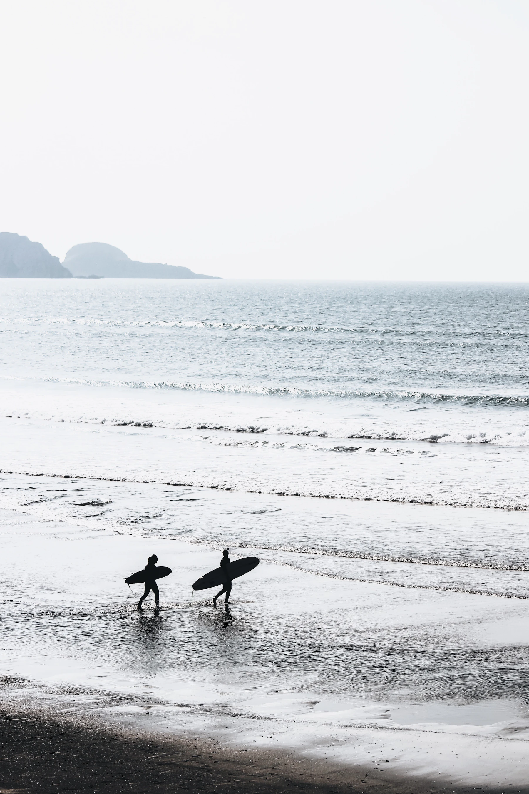 Two people carrying surfboards along a beach