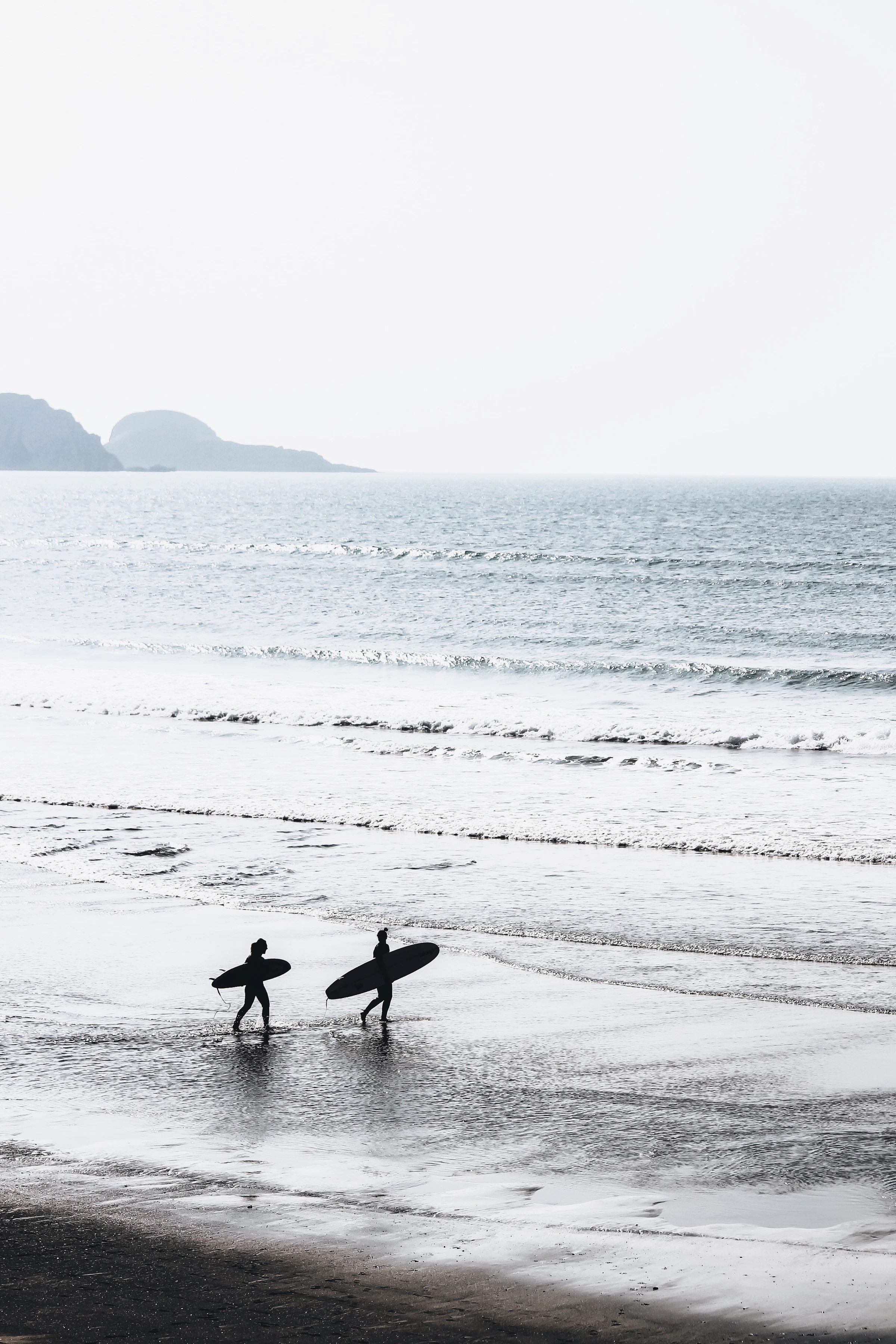 Two people carrying surfboards along a beach