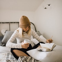 woman in striped shirt sitting on bed while writing