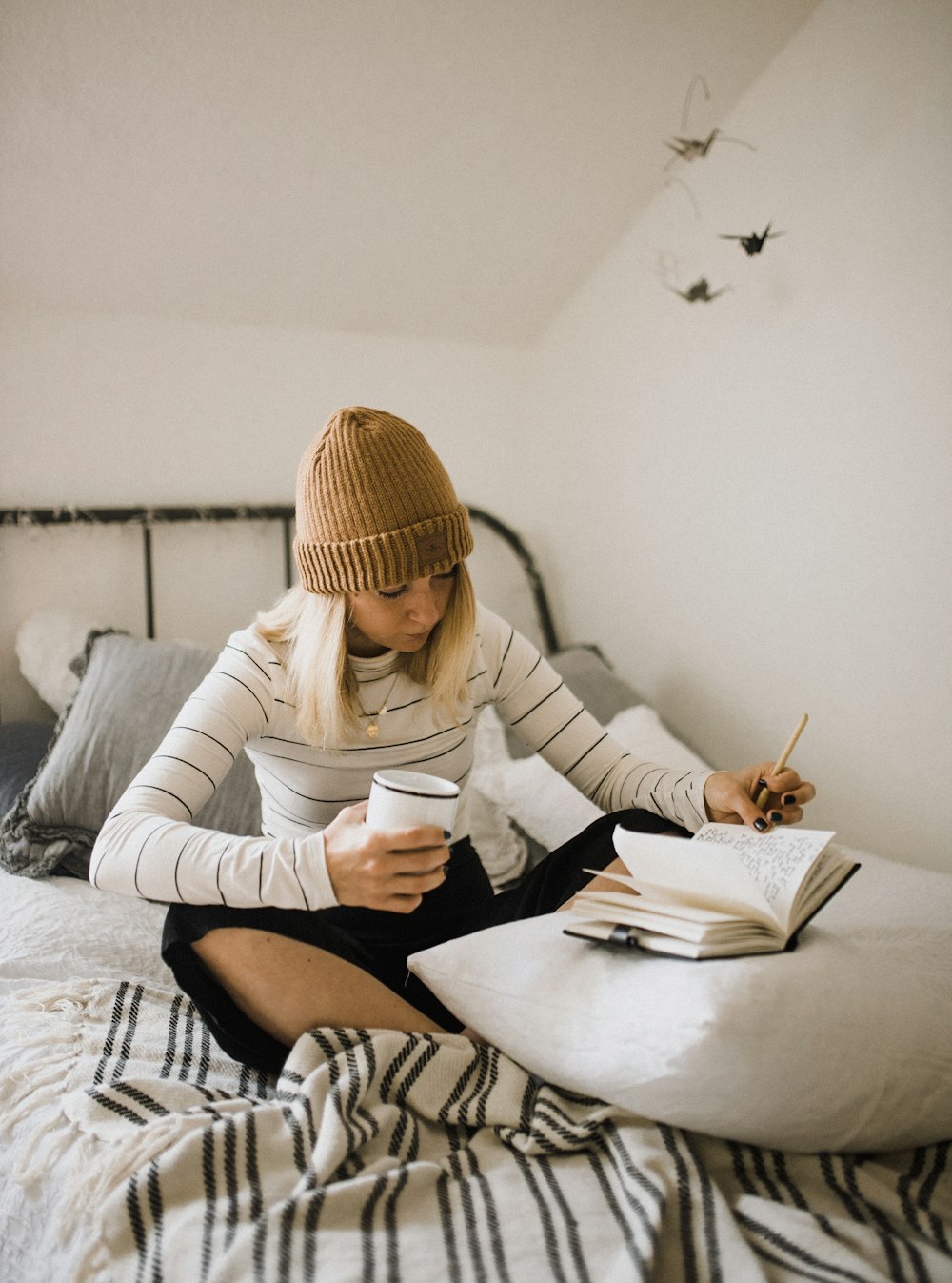 mulher na camisa listrada sentada na cama enquanto escreve