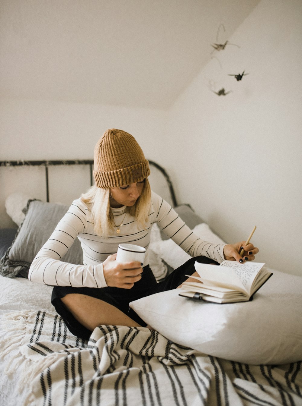 Femme en chemise rayée assise sur le lit tout en écrivant