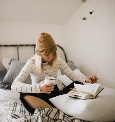 woman in striped shirt sitting on bed while writing