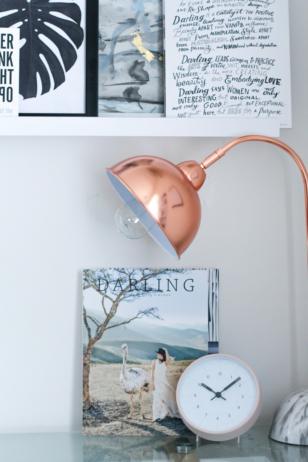 lampe de bureau marron à côté d’une horloge de table blanche et d’un cadre Darling
