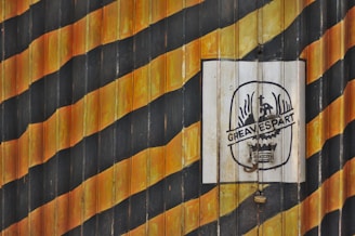 Wooden panels are painted in alternating black and orange diagonal stripes, creating a striking pattern. A white sign with an emblem and the text 'GREAVESPART' is placed on the right side.