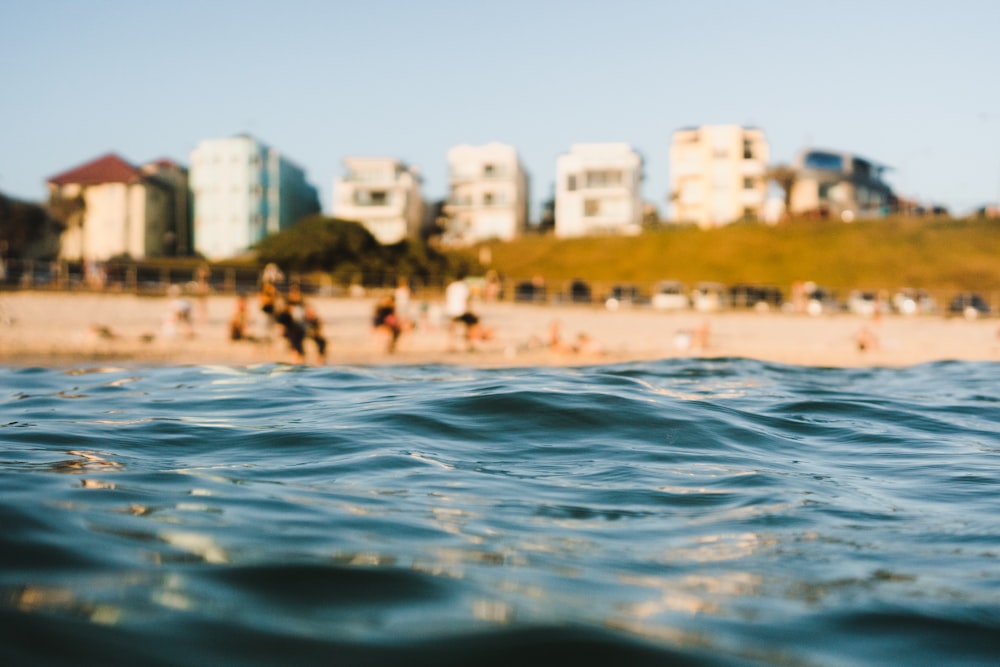 Selektive Fokusfotografie des Meeres in der Nähe von Menschen, die auf Sand stehen