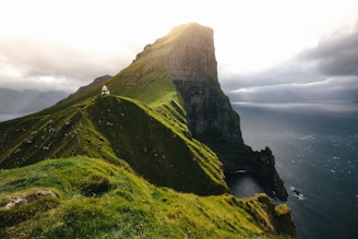 green mountain surrounded by ocean under cloudy sky during daytime