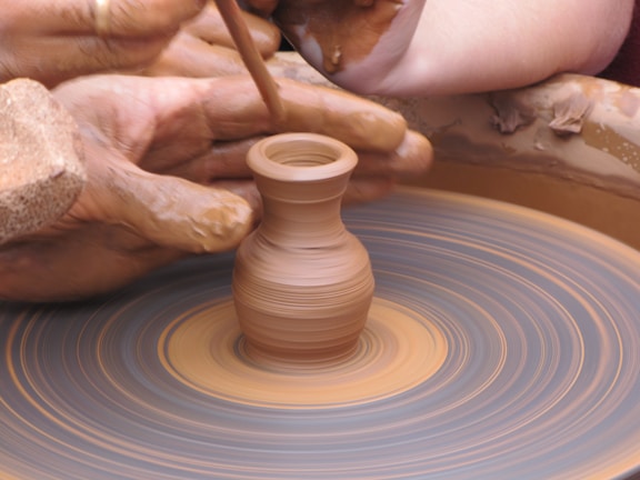 Close-up of a potter's hands molding wet clay on a spinning wheel.