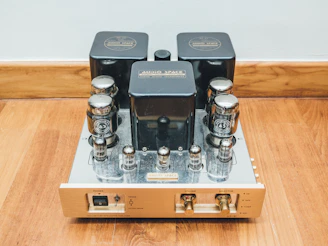 Close-up of a vintage tube preamp glowing warmly beside a classic Tone Bender fuzz pedal on a dark wooden studio desk.