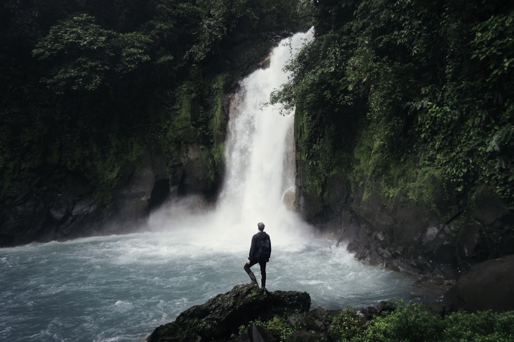 man standing on cliff near falls