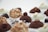 An assortment of gourmet truffles arranged on a white background. Each truffle is uniquely decorated, some with nuts, others with cocoa powder, and some with white chocolate coatings. They are placed in paper wrappers, enhancing their presentation.