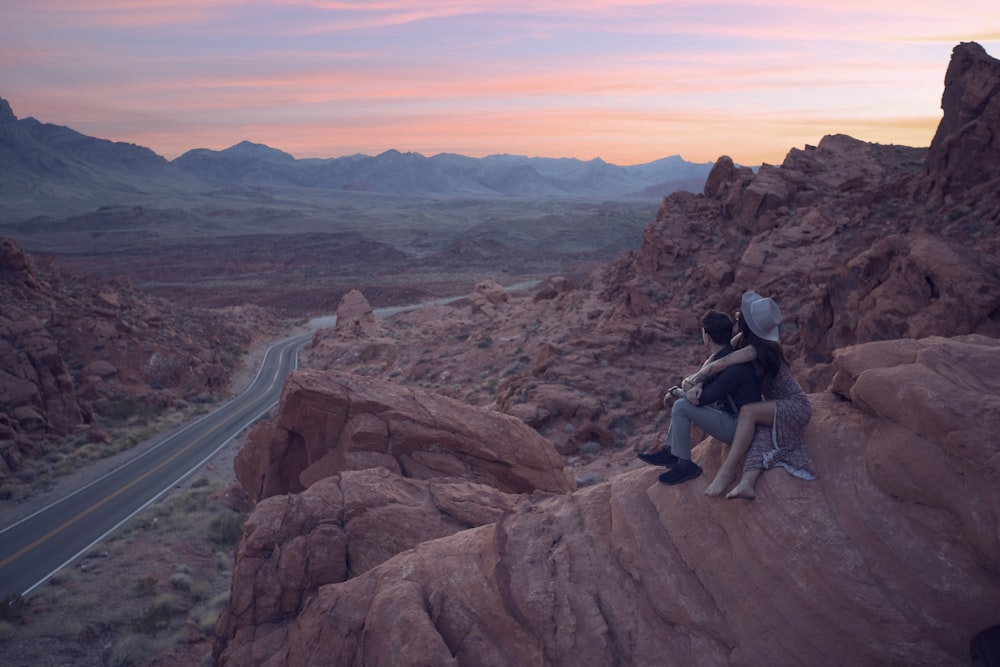 two people sitting on top of a large rock