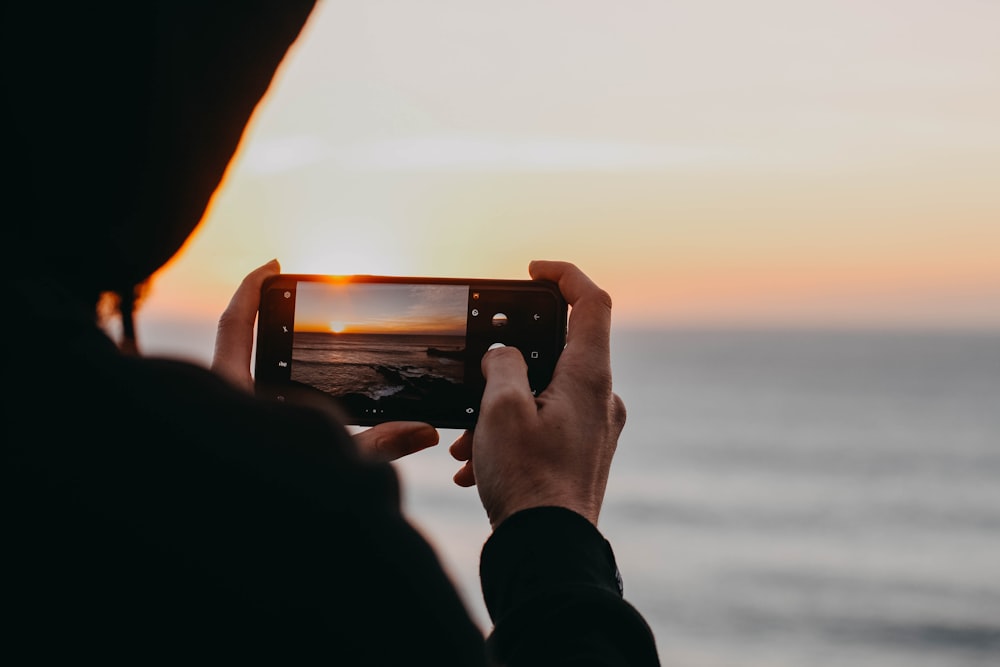 Foto di una persona che tiene uno smartphone nero in procinto di catturare il mare