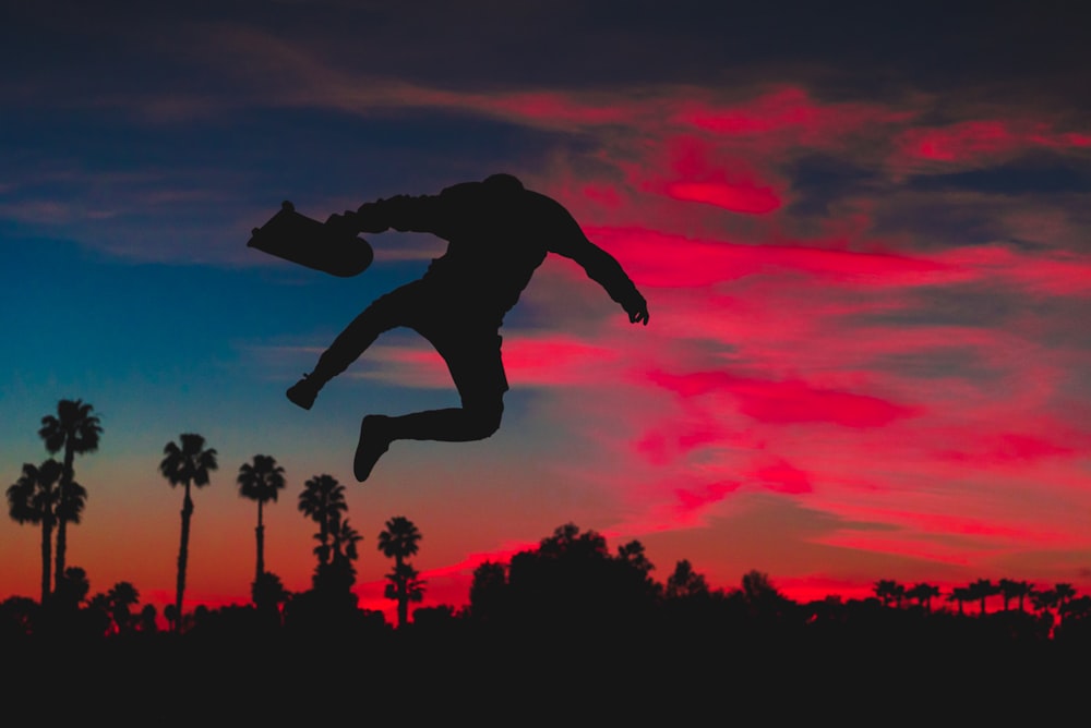 silhouette of person jumping while holding skateboard