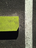 A neon green concrete curb parallels a white painted line on a dark asphalt surface, creating a strong contrast between the vibrant color and the muted ground.