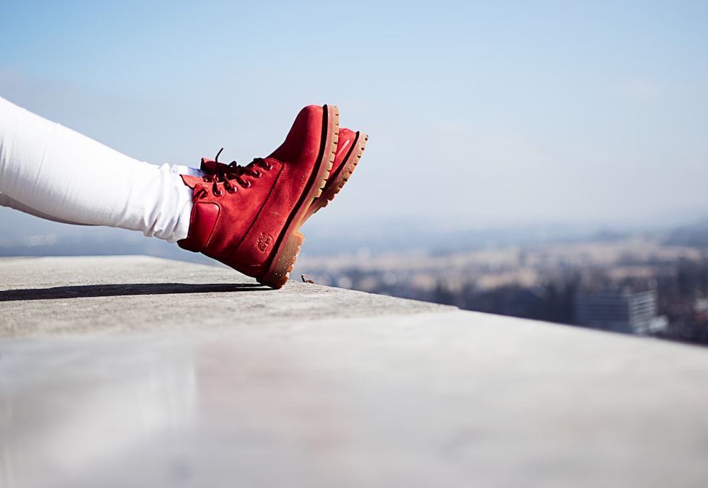 person wearing pair of red boots sitting on building top