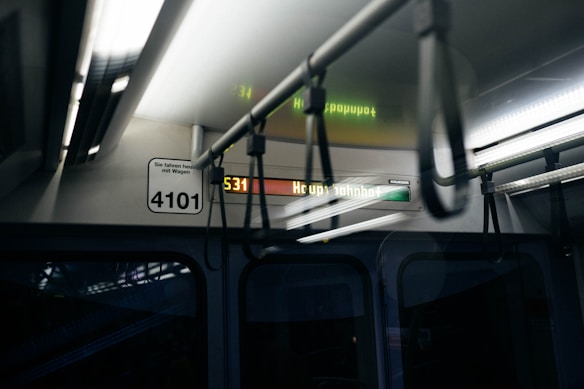 Interior of a public transportation vehicle with overhead handrails and an illuminated destination sign displaying 'Hauptbahnhof'. The vehicle's number 4101 and a notice in German are visible. The lighting is dim, adding to a reflective atmosphere.
