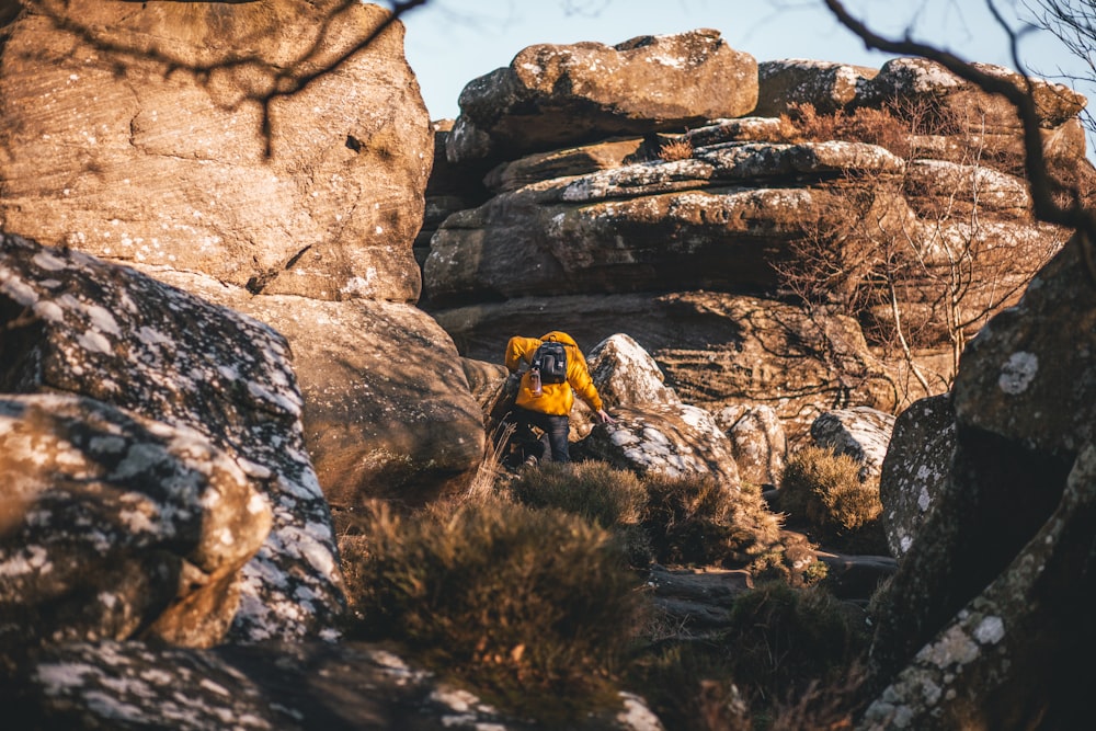 노란 재킷을 입은 사람이 낮에 산 근처의 바위 위를 걷고 있다.