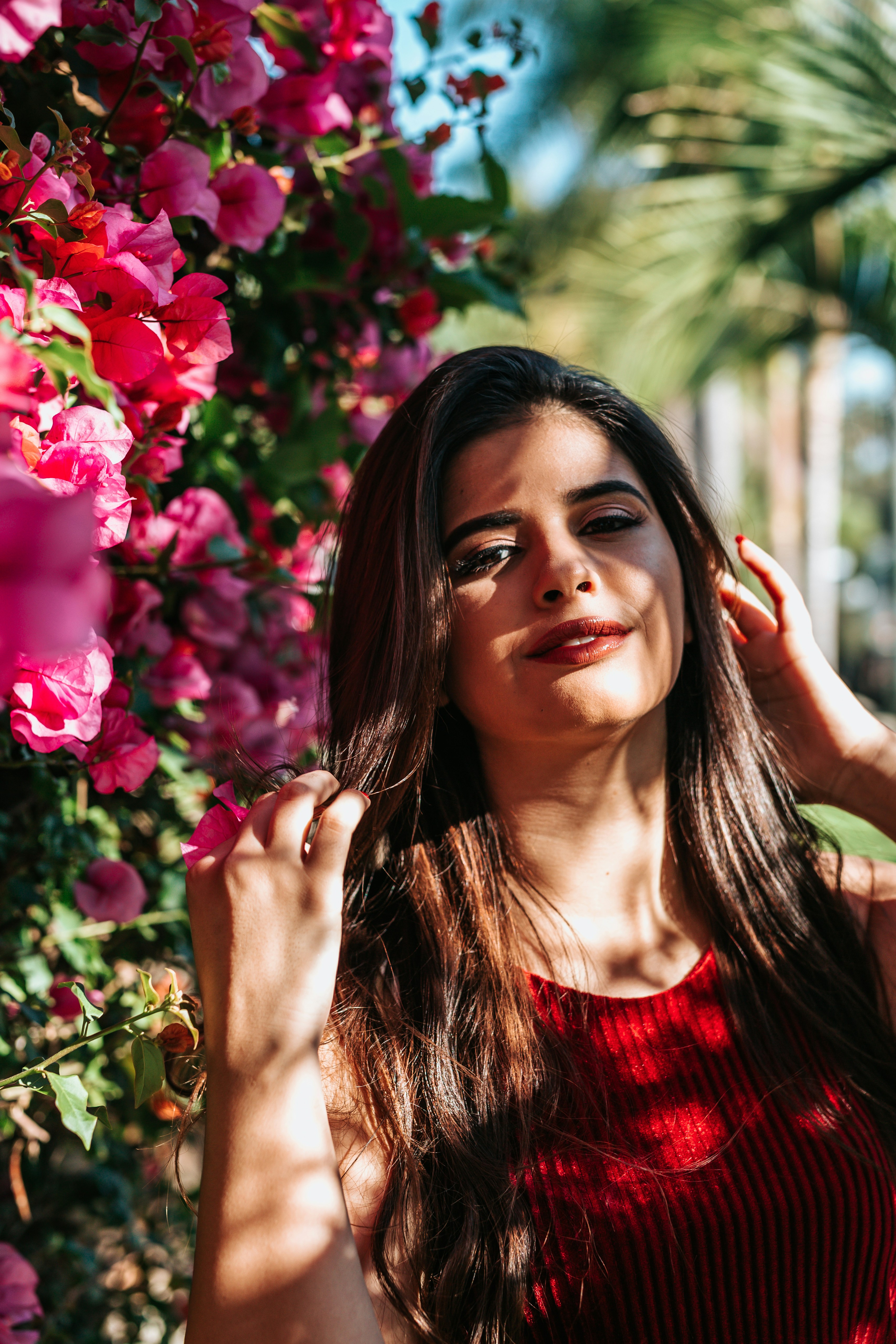 selective focus photography of woman wearing red crew-neck sleeveless top beside pink flowers