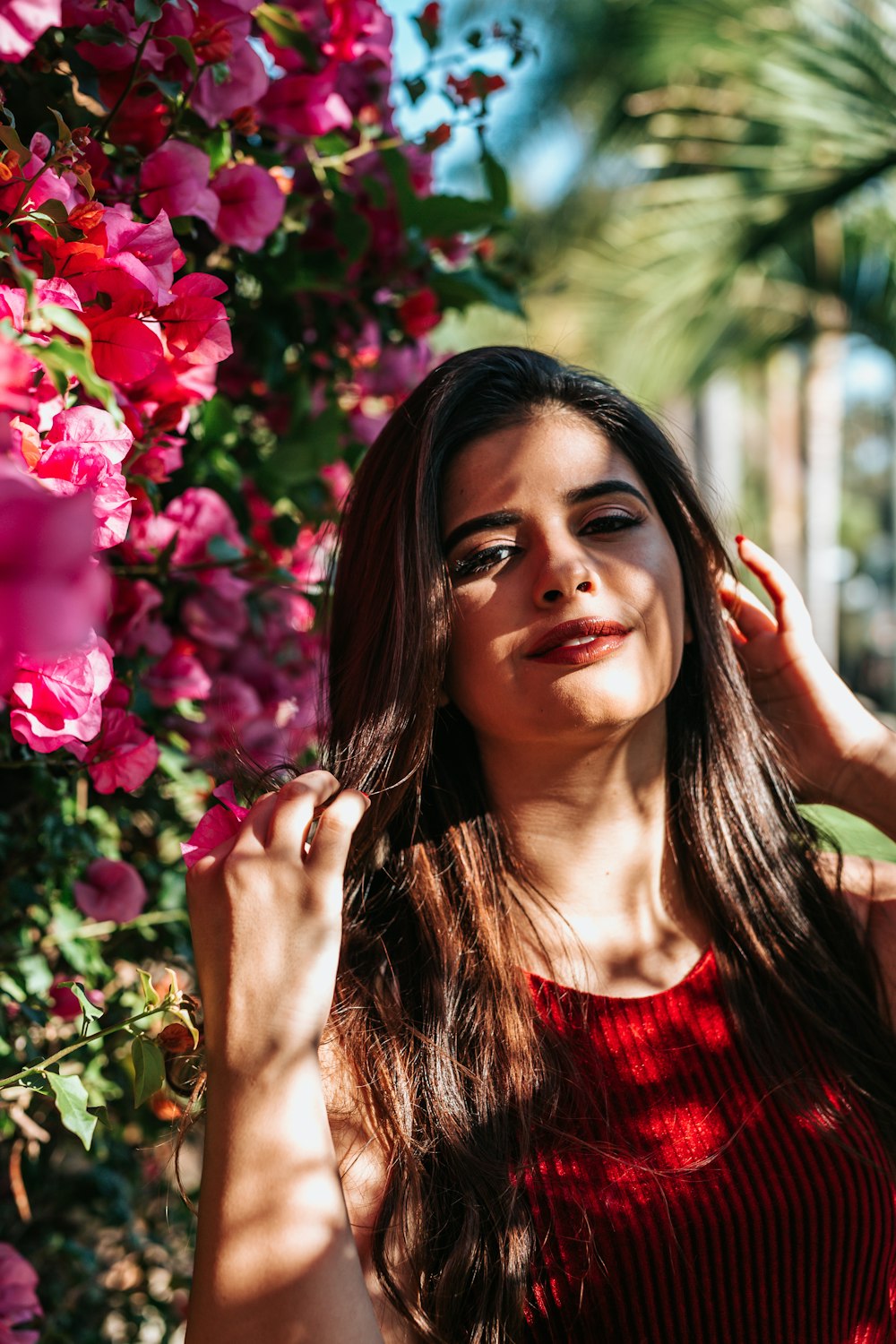 selective focus photography of woman wearing red crew-neck sleeveless top beside pink flowers