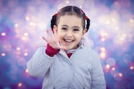 A close-up of a young girl in Jordan smiling brightly as she performs a scene with expressive hand gestures.