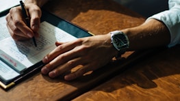 person writing on paper leaning on brown table