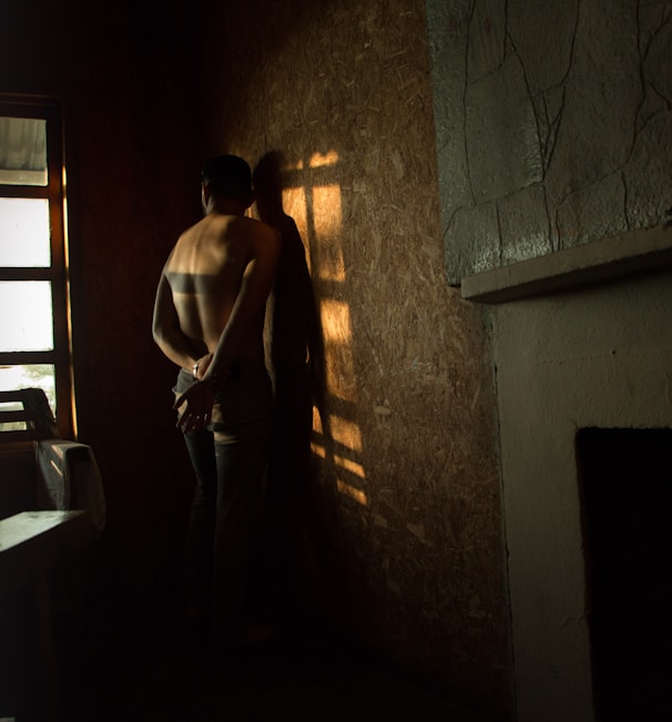 topless man facing on wall beside bed inside the room