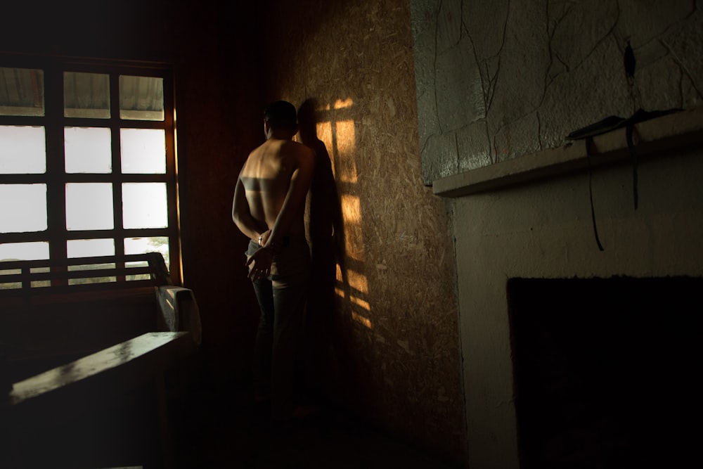 topless man facing on wall beside bed inside the room