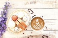 Elegant coffee cup with latte art beside a small plate of handcrafted sweets on a sleek marble surface.