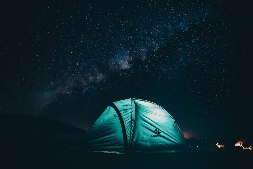 밤에는 별이 빛나는 하늘 아래 내부에 빛이 있는 녹색과 검은색 텐트