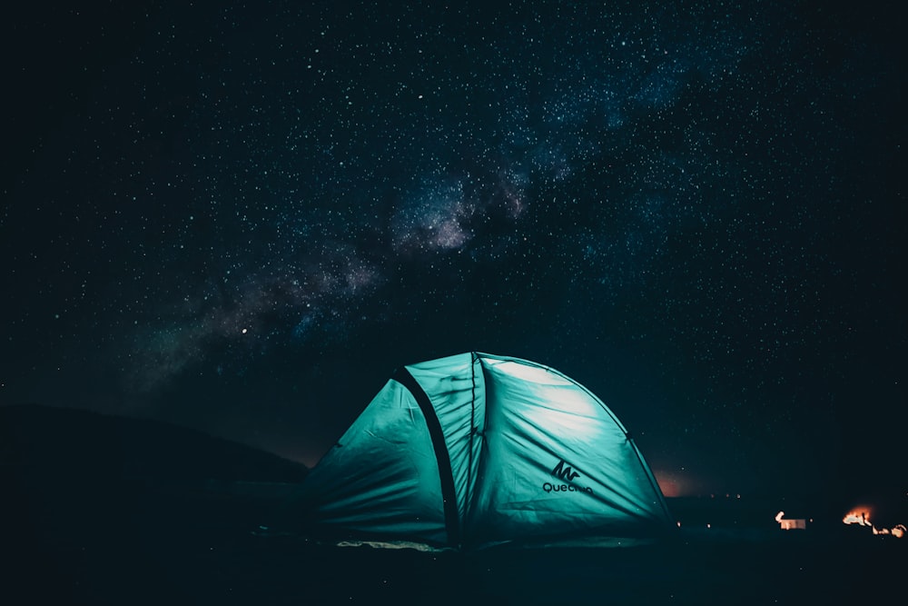 Tienda verde y negra con luz en el interior bajo el cielo estrellado durante la noche