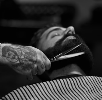 grayscale photography of person holding scissor clipping man's beard