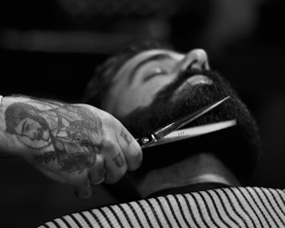 grayscale photography of person holding scissor clipping man's beard