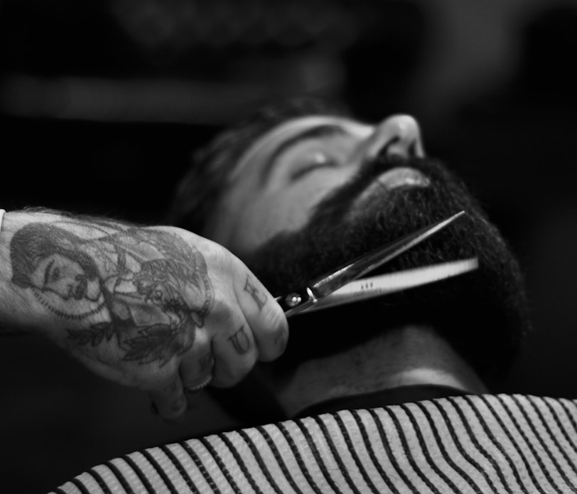 grayscale photography of person holding scissor clipping man's beard