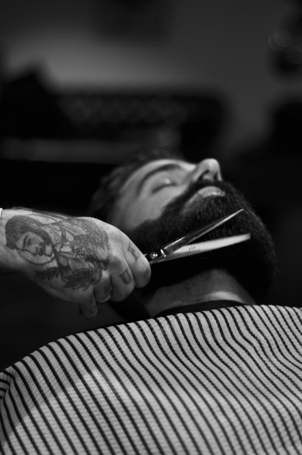 fotografia em tons de cinza da pessoa segurando tesoura cortando a barba do homem