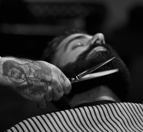 grayscale photography of person holding scissor clipping man's beard