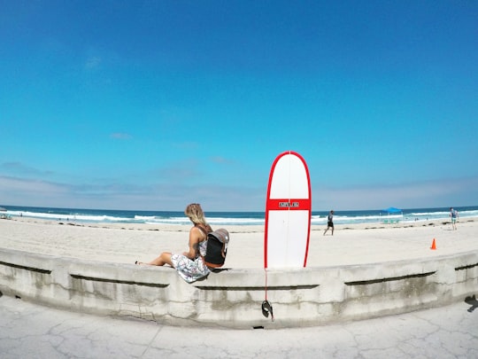 woman sitting on white concrete barrier beside skimboard during daytime in San Diego United States