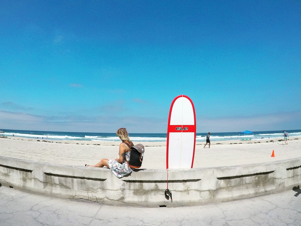 woman sitting on white concrete barrier beside skimboard during daytime